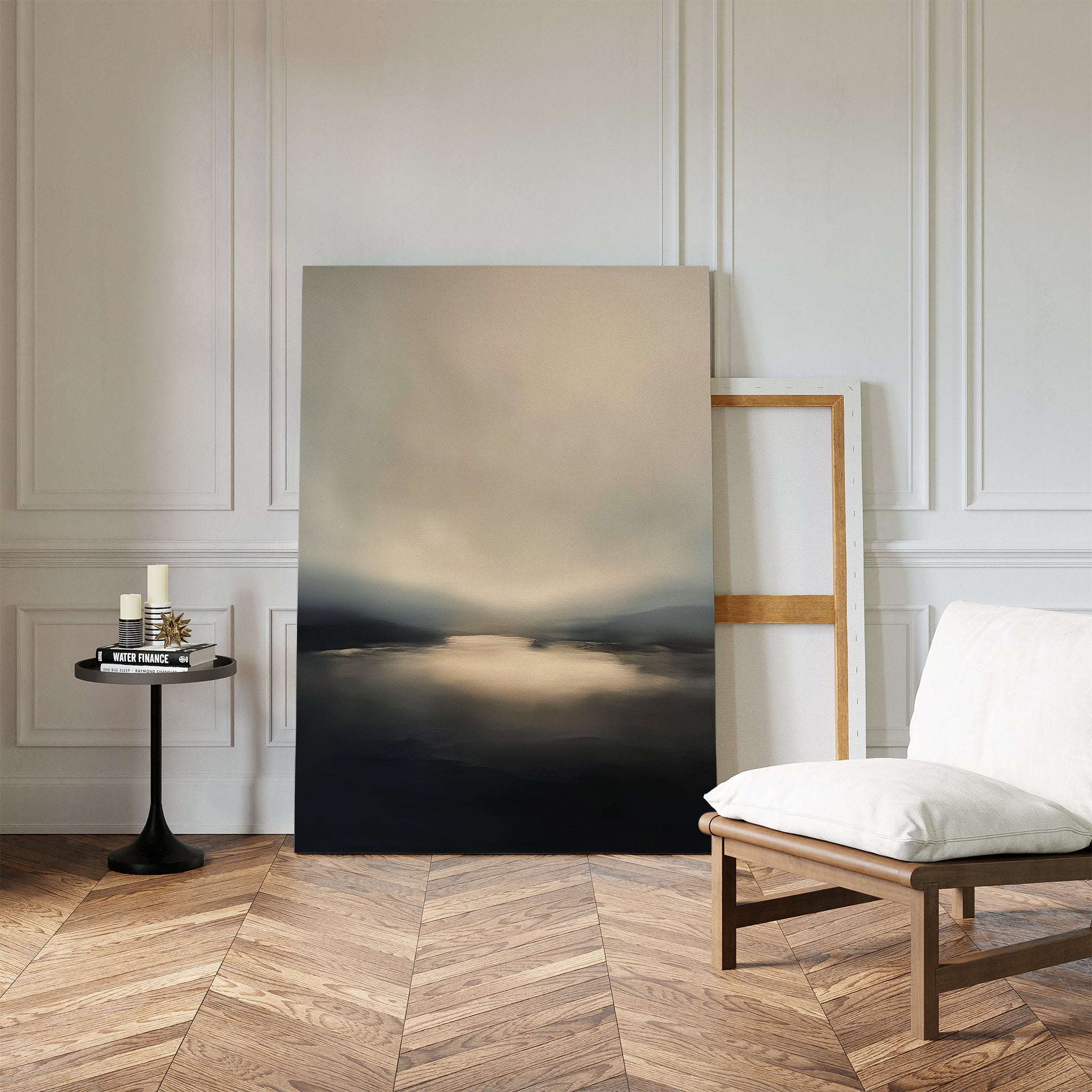 A minimalist room with chevron wood floors features the Golden Fog Horizon Canvas Art - Vertical leaning against a white paneled wall, beside a modern white chair and a small black side table holding candles and books.