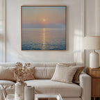 A modern living room features a beige sofa with light cushions, a side table and lamp, dried flowers in a vase, and the Golden Reflection Canvas Art - Square depicting a serene ocean sunset hanging on the wall.