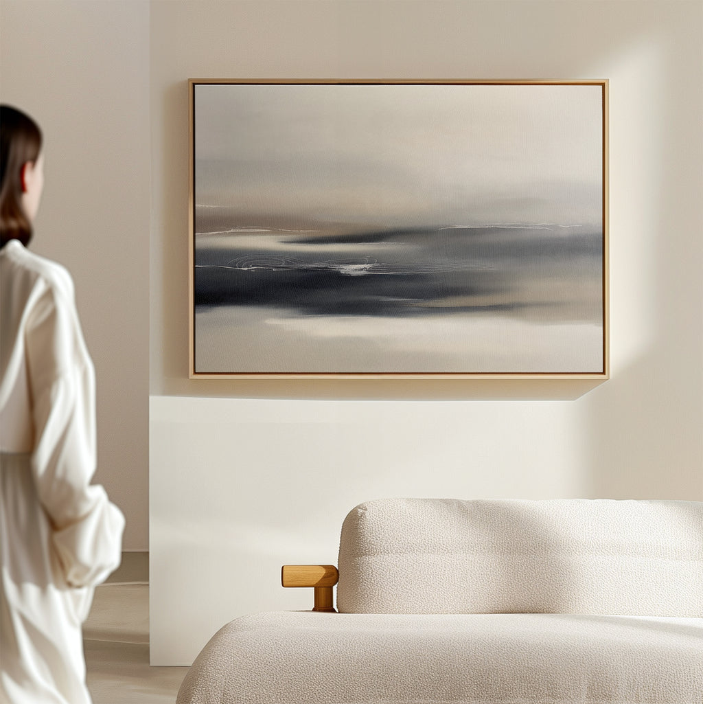 A person in a white shirt stands in a bright, minimalist room, admiring the Grey Ripples Canvas Art - Horizontal with its soft gray and beige tones displayed above a modern textured sofa—perfect inspiration for stylish living rooms.