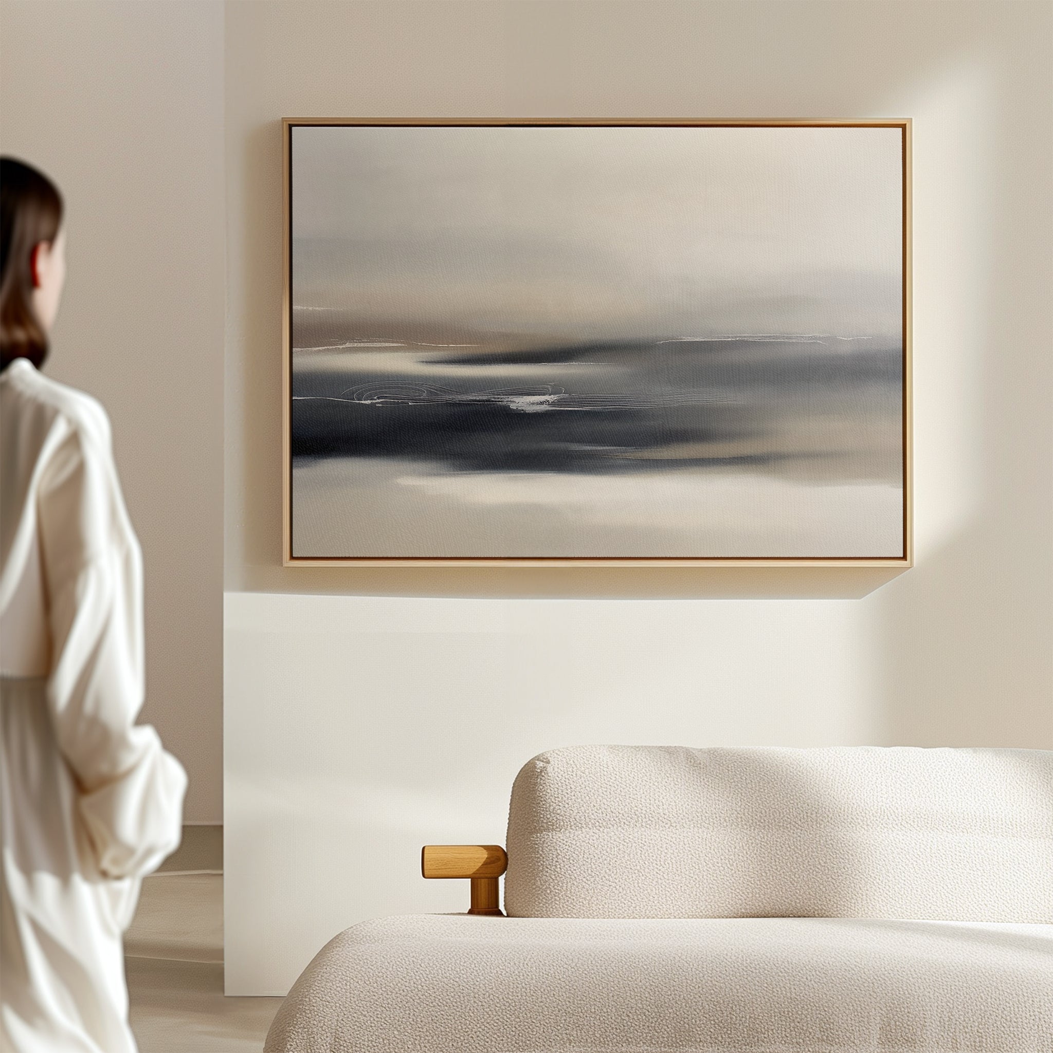 A person in a white shirt stands in a bright, minimalist room, admiring the Grey Ripples Canvas Art - Horizontal with its soft gray and beige tones displayed above a modern textured sofa—perfect inspiration for stylish living rooms.
