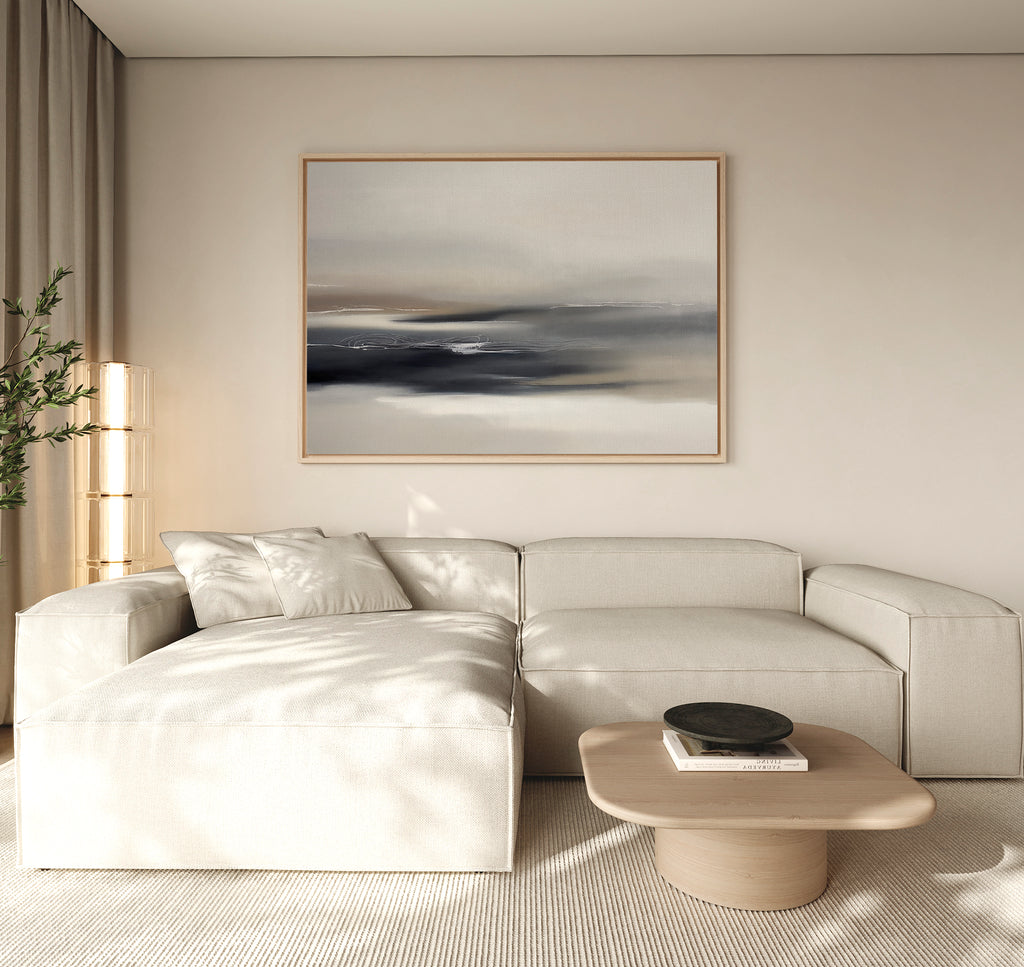 A modern, minimalist living room with a beige sectional sofa, a light wooden coffee table with a black bowl, tall lamp, potted plant, and the Grey Ripples Canvas Art - Horizontal hanging above the sofa.