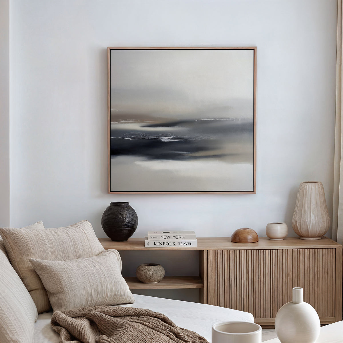 A minimalist living room features a beige sofa with striped pillows, a wooden sideboard with vases and books, and the Grey Ripples Canvas Art - Square in muted tones on a white wall. Soft natural light fills the space.