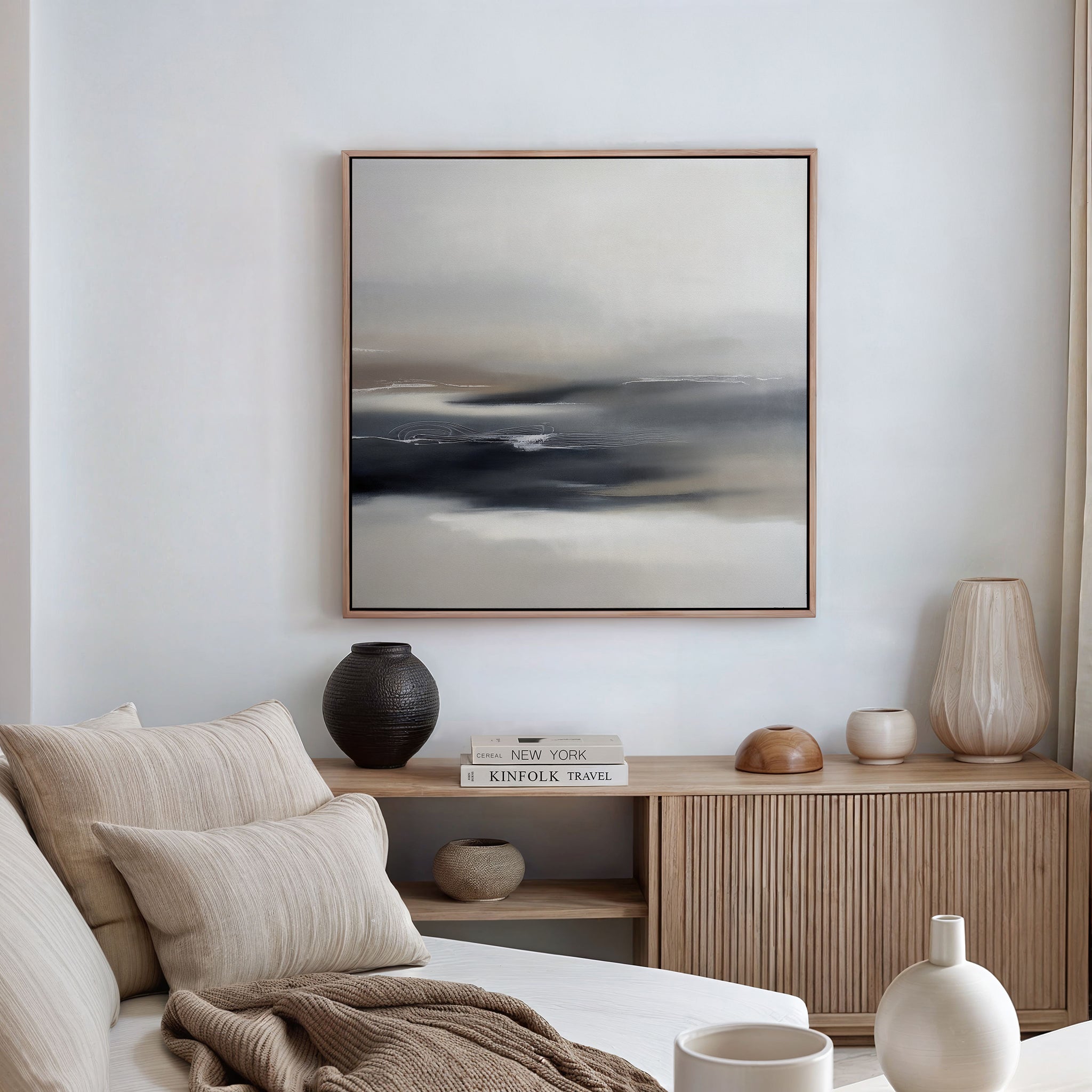 A minimalist living room features a beige sofa with striped pillows, a wooden sideboard with vases and books, and the Grey Ripples Canvas Art - Square in muted tones on a white wall. Soft natural light fills the space.