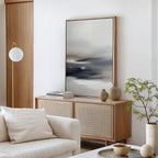 A modern living room featuring a light wood sideboard, the Grey Ripples Canvas Art - Vertical, decorative vases, stacked books, a potted plant, a white sofa with a cushion, and a round floor lamp against a white wall.
