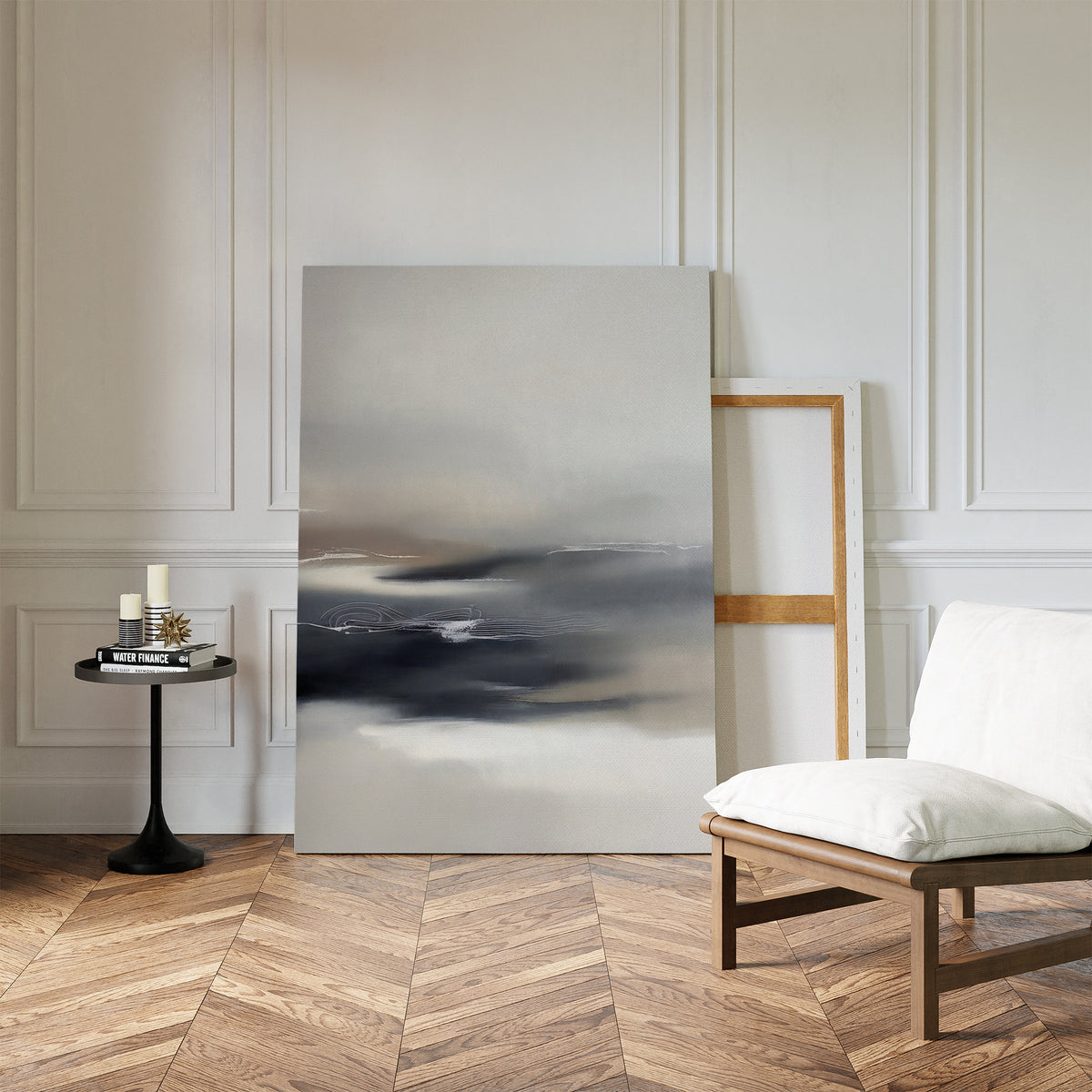 A minimalist room with herringbone wood floors, a modern white chair, a small black round table with candles and books, and the Grey Ripples Canvas Art - Vertical leaning against a white paneled wall—perfect for modern living rooms.