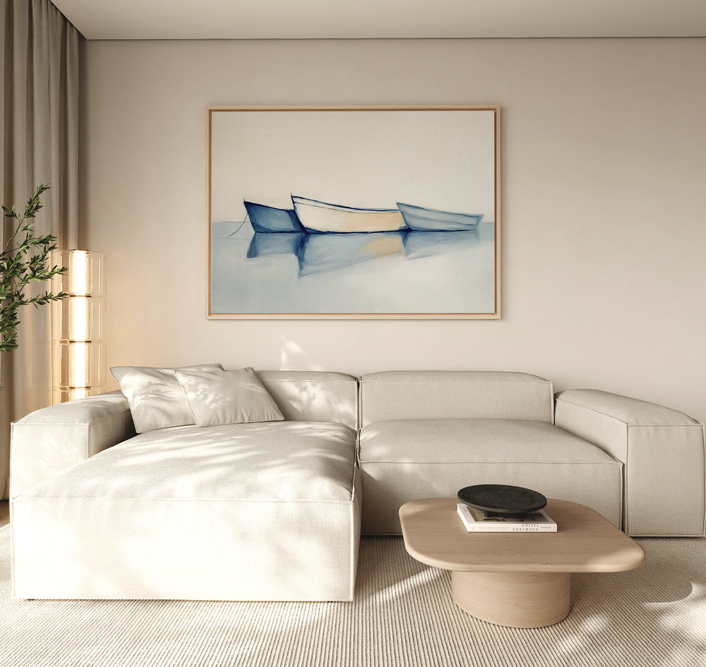 A modern living room with a light beige sectional, round wooden coffee table, and calming decor featuring Harbor Rest Canvas Art - Horizontal. Soft natural light streams in from the left, and a green plant sits in the corner.