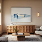 A cozy living room with a wooden sideboard, low coffee table, neutral sofa, and the Harbor Rest Canvas Art - Horizontal featuring three blue boats above the sideboard. Soft lighting and minimal decor add calm to this serene space.