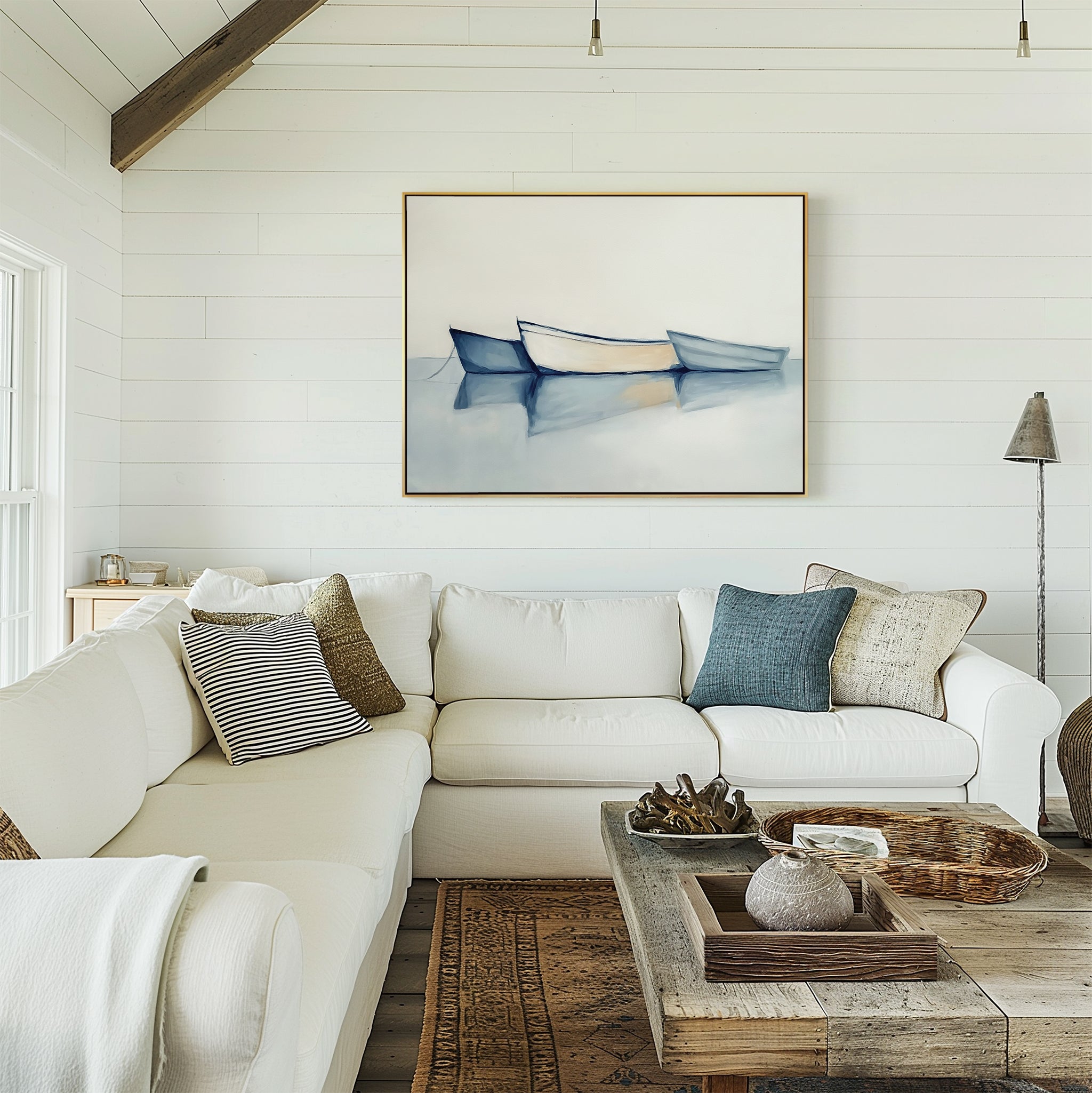 Bright living room with a white sectional and rustic coffee table. The Harbor Rest Canvas Art - Horizontal, showing two blue boats on calm water, brings a serene touch as sunlight pours in from the left window.