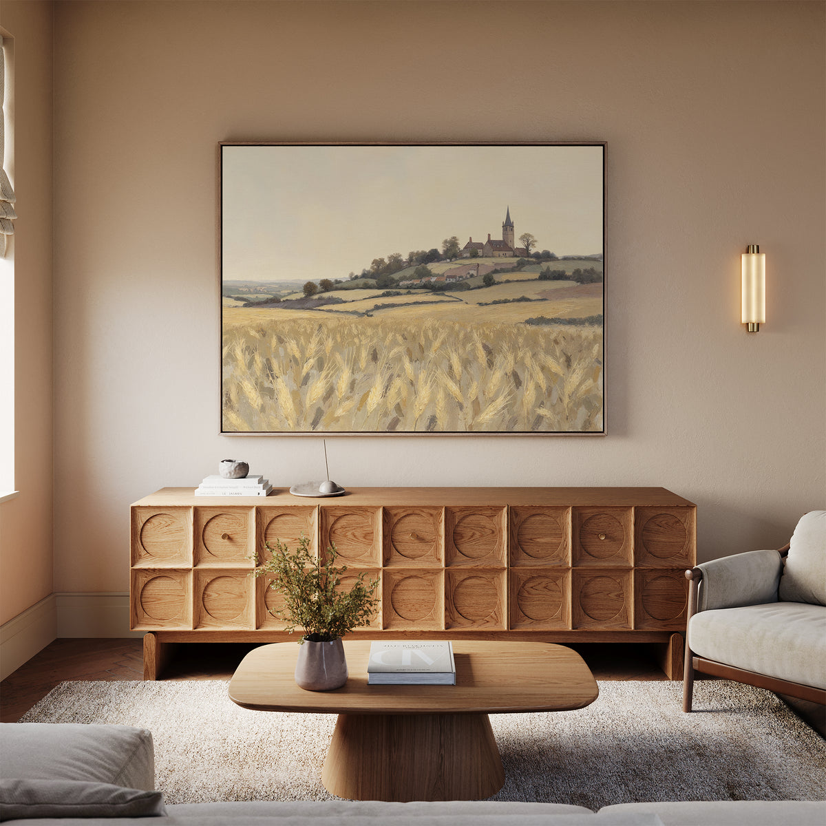 A cozy living room with a wooden coffee table, credenza, neutral sofa, light rug, and the "Harvest Chapel Canvas Art - Horizontal" depicting a village scene. A lamp and vase on the credenza add to the softly lit, inviting atmosphere.