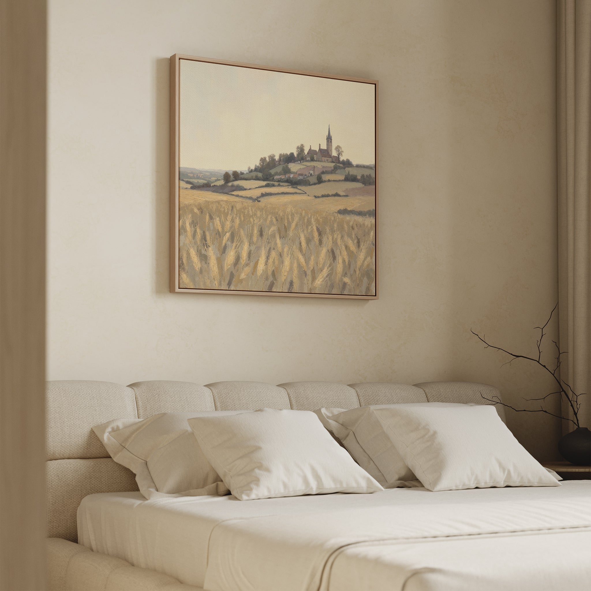 A cozy bedroom with a beige upholstered bed and white pillows, highlighted by the Harvest Chapel Canvas Art - Square above the bed, which depicts a hillside village and wheat fields for a rustic touch.