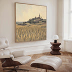 A modern living room features a white lounge chair and ottoman, wooden side table with a white lamp, and the Harvest Chapel Canvas Art - Square adding rustic charm to the space.