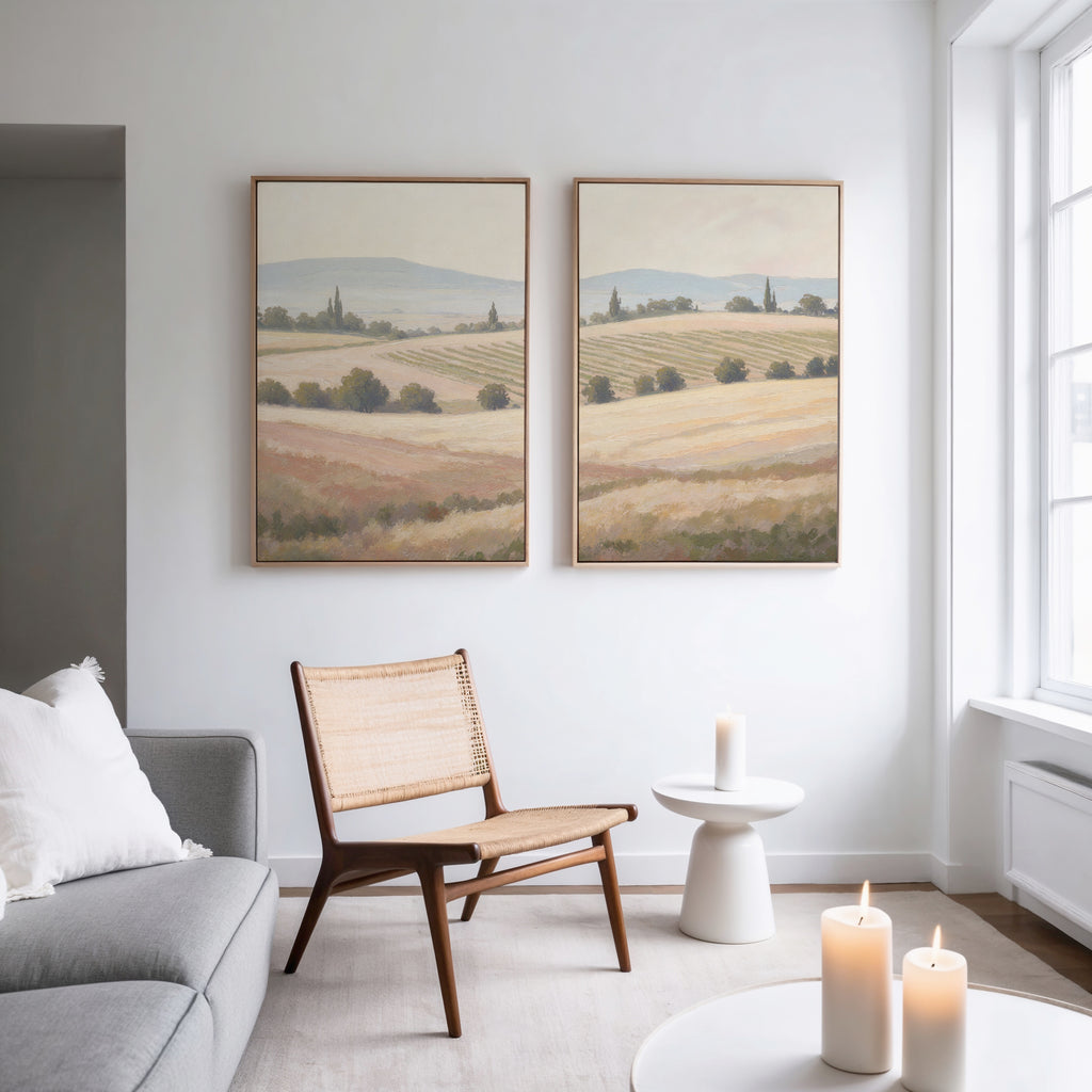 A modern minimalist living room featuring a woven chair, white side table, candles, gray sofa, and Harvest Fields - Set of 2 canvas paintings on a white wall, with natural light streaming through large windows.