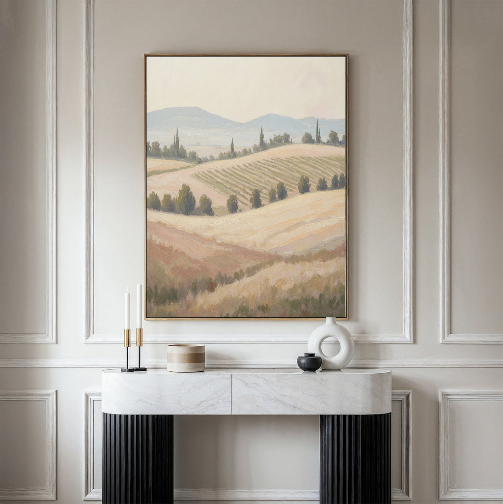 The Harvest Fields Canvas Art - Vertical, featuring rolling hills and fields, hangs above a marble console table with minimalist vases and candles against an elegant paneled wall.