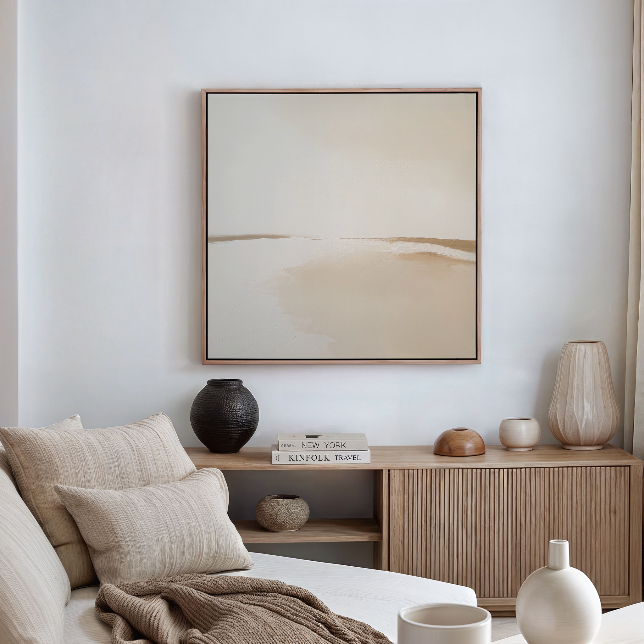 A minimalist living room in neutral tones features a beige sofa with pillows, a wooden sideboard with books and vases, and the Serene Expanse Abstract Canvas Art, adding an elegant touch with its soft, muted colors.