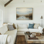 A cozy living room with a white sectional sofa, assorted pillows, wooden coffee table, and the Heron's Morning Canvas Art - Horizontal displayed on a white shiplap wall. Natural light enhances the serene and inviting space.
