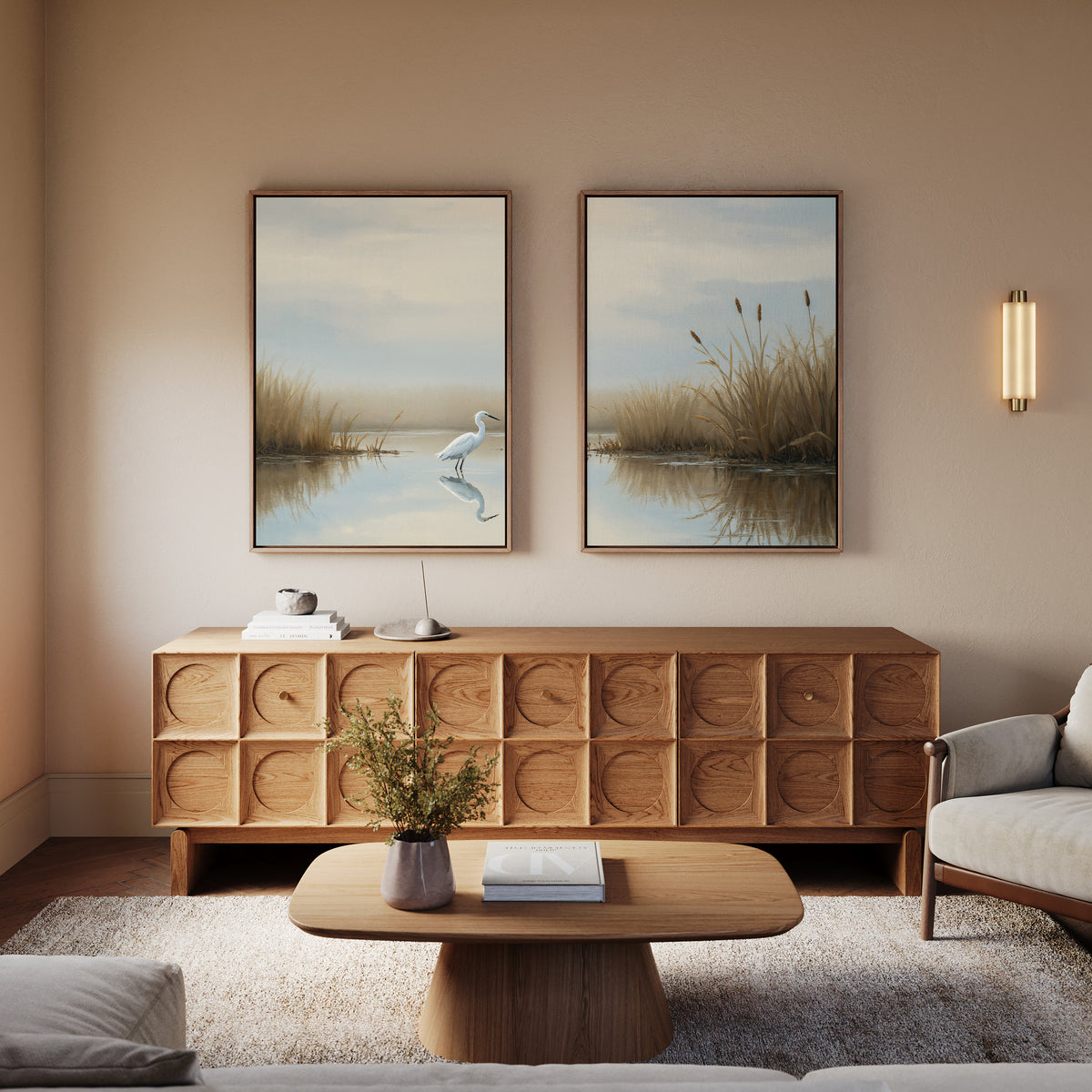 A cozy living room features a wooden sideboard and coffee table, a light sofa, and "Heron's Morning - Set Of 2" wall art on the beige wall. A small plant and books decorate the tables.