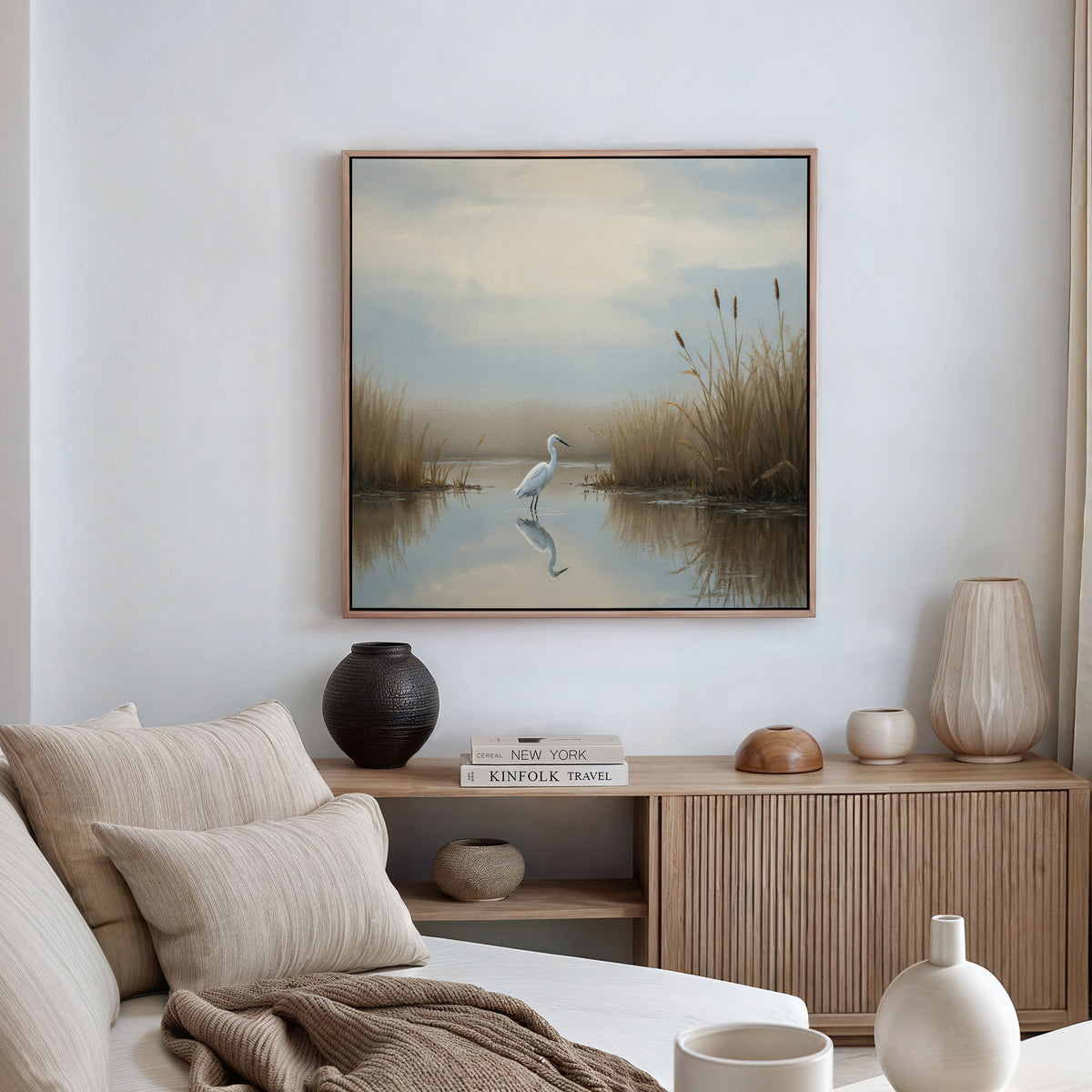 A tranquil living room with neutral hues showcases the Heron's Morning Canvas Art - Square above a wooden console decorated with vases and books, while a beige sofa sits in front.