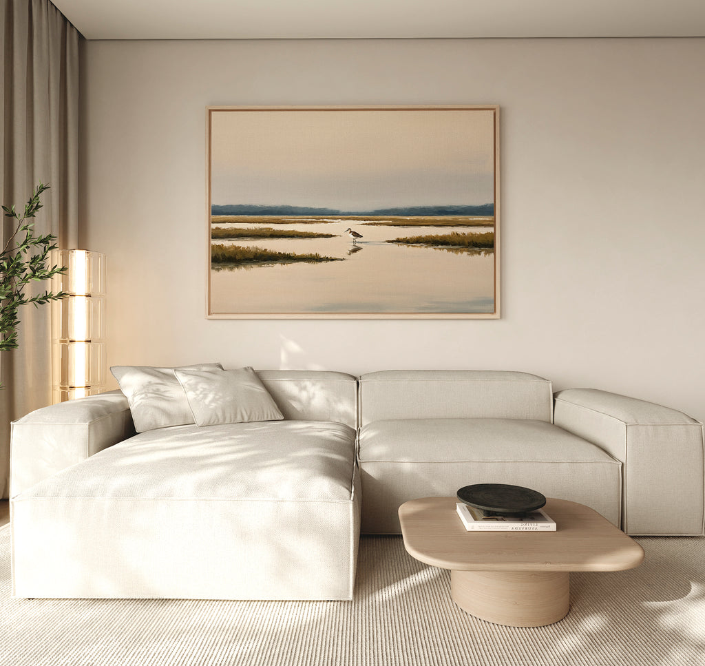 A modern living room featuring a light beige sectional sofa, a wooden coffee table with books and a bowl, and the Marsh Bird Canvas Art - Horizontal displayed above the sofa for a tranquil touch.