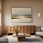 A cozy living room with a beige sofa, wooden coffee table, and a patterned sideboard. Above the sideboard hangs the Marsh Bird Canvas Art - Horizontal, illuminated by a sconce light on the wall.
