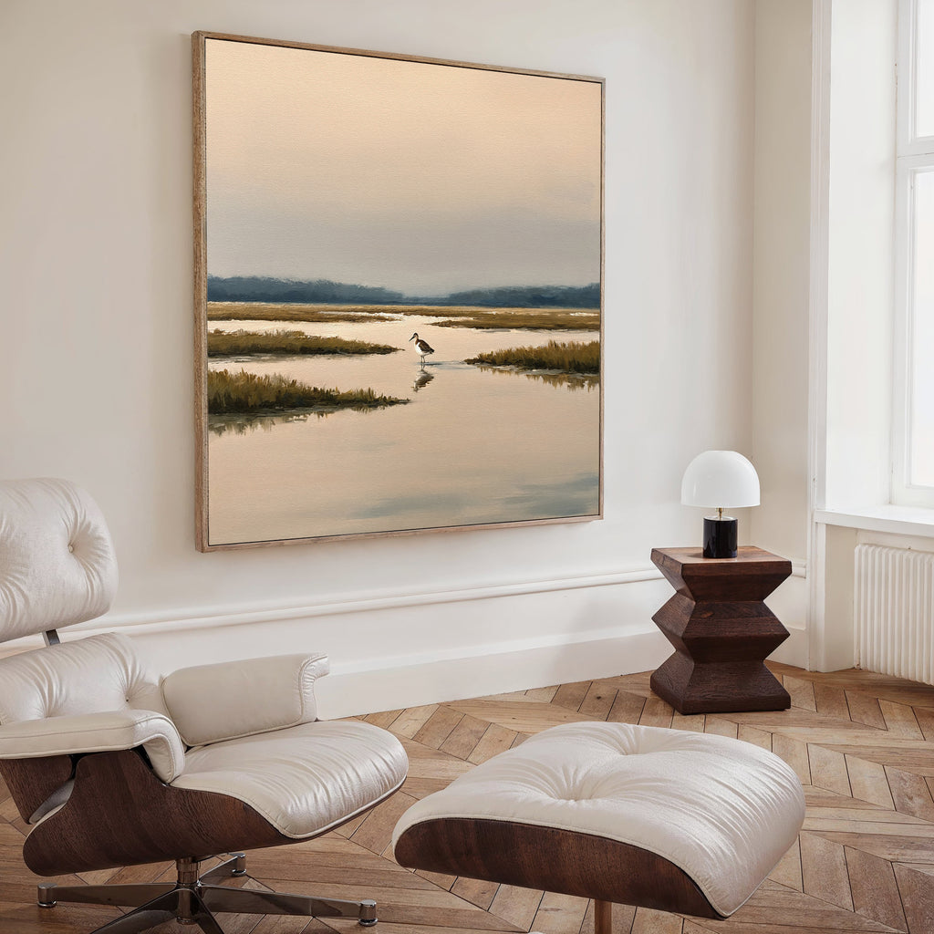 A stylish living room featuring a modern white lounge chair and ottoman, a wooden side table with a round lamp, and the Marsh Bird Canvas Art - Square displayed elegantly on the wall.