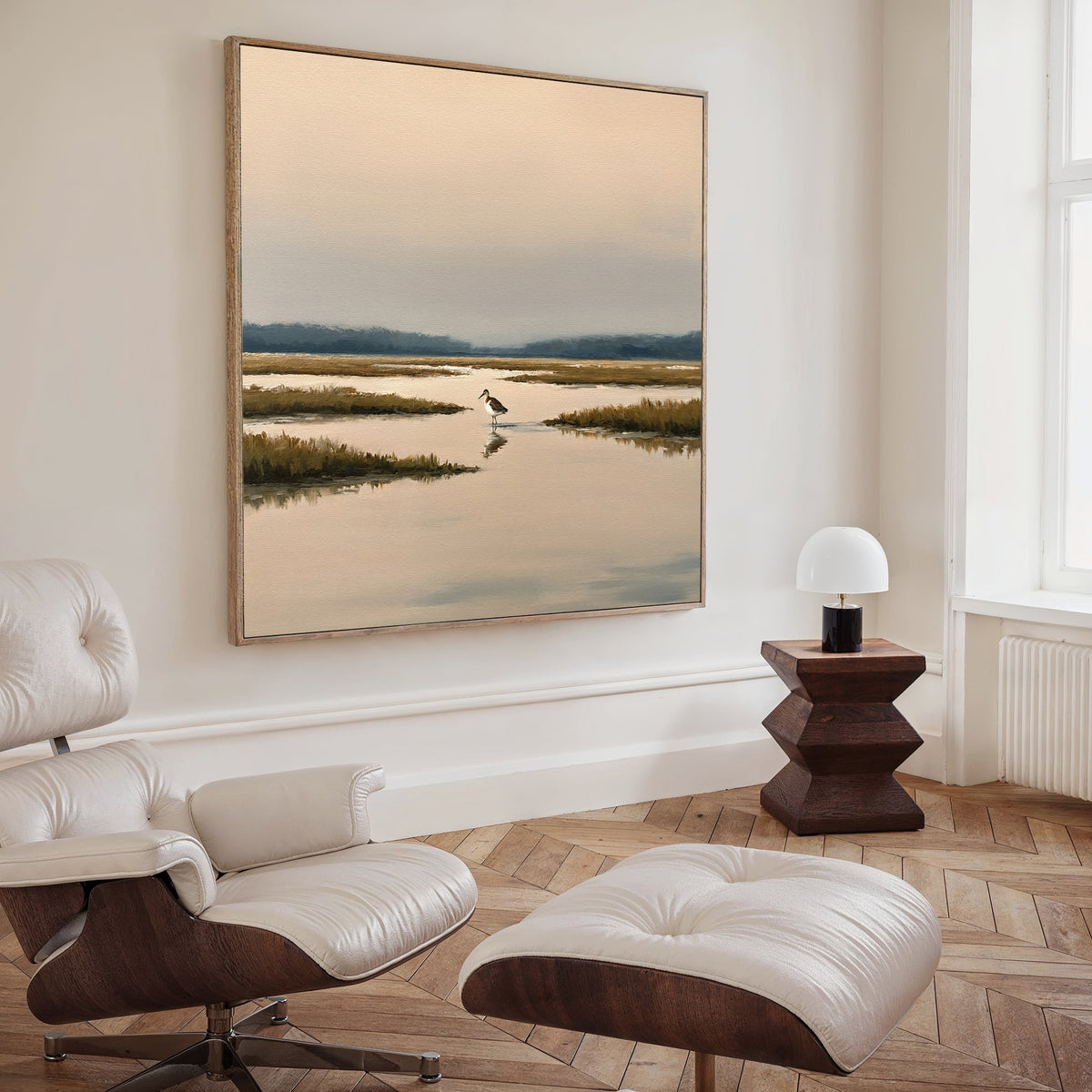 A stylish living room featuring a modern white lounge chair and ottoman, a wooden side table with a round lamp, and the Marsh Bird Canvas Art - Square displayed elegantly on the wall.