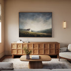 A cozy, modern living room features a wooden sideboard topped by the Highland Solitude Canvas Art - Horizontal, a round coffee table, neutral sofas, and soft natural light from a window for a touch of rustic tranquility.