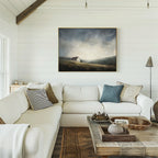 A cozy living room with a white sectional and rustic coffee table is centered around the Highland Solitude Canvas Art - Horizontal, a moody landscape that adds rustic tranquility to the white shiplap wall.