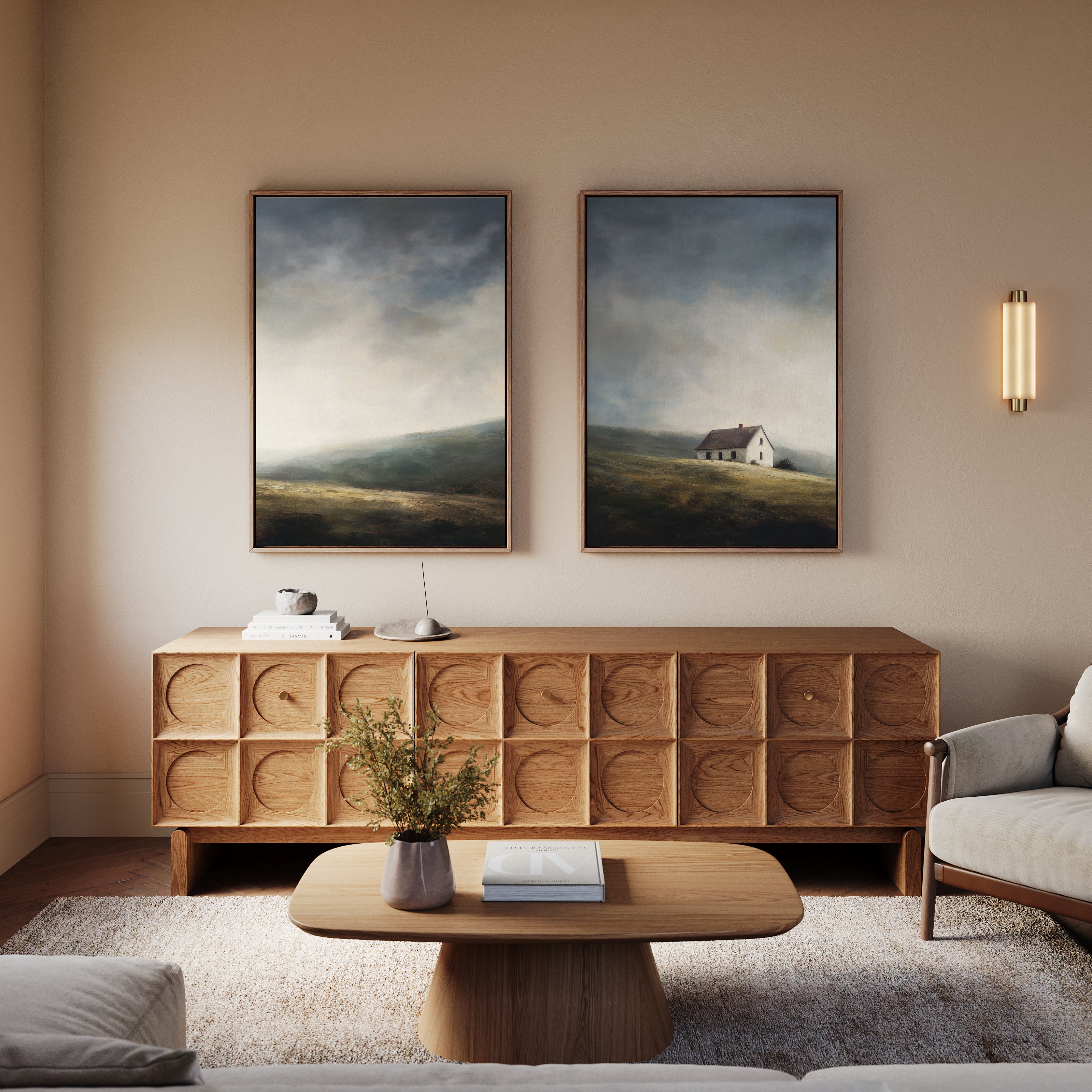 A cozy living room features a wooden sideboard with geometric patterns, a matching coffee table, a light gray sofa, and two framed moody landscape paintings above—the Highland Solitude - Set of 2.