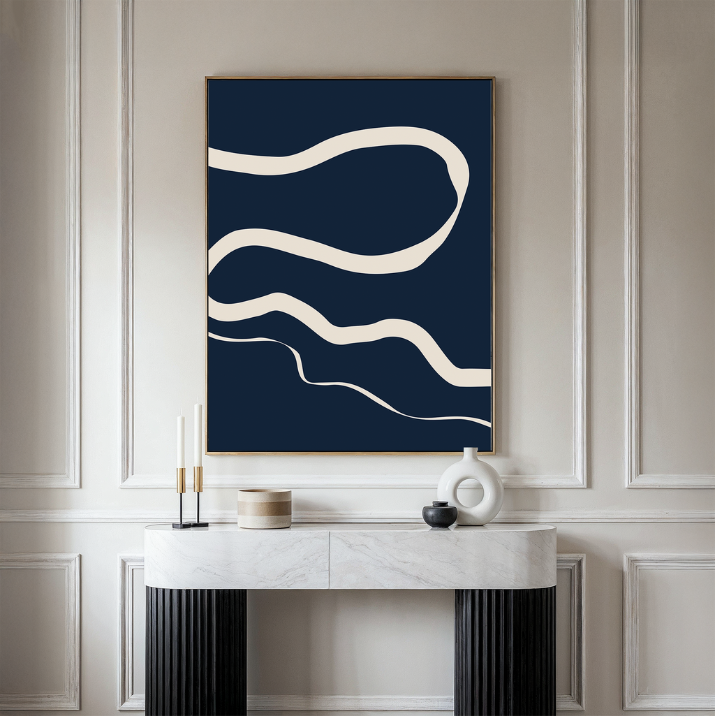 A modern interior showcases a minimalist console table with decor accents beneath the Blue Tranquility Abstract Canvas Art, featuring wavy white lines on a dark blue background, set against elegant light-paneled walls for a sophisticated touch.