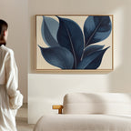 A person in a white shirt stands in a modern, minimalistic room, admiring the Indigo Depths Canvas Art - Horizontal featuring abstract blue leaves, which hangs above a beige sofa on a light-colored wall.