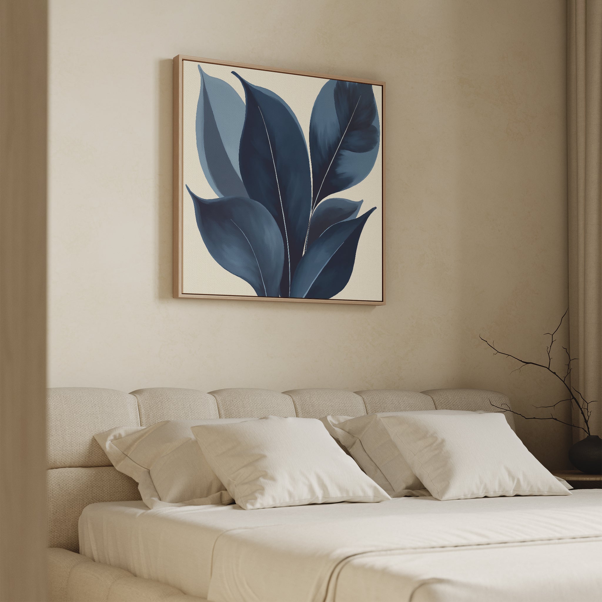 A minimalist bedroom features a beige upholstered bed with white bedding and four pillows. Above the bed hangs the Indigo Depths Canvas Art - Square, showcasing large blue leaves. A bare branch in a vase sits on the side table.