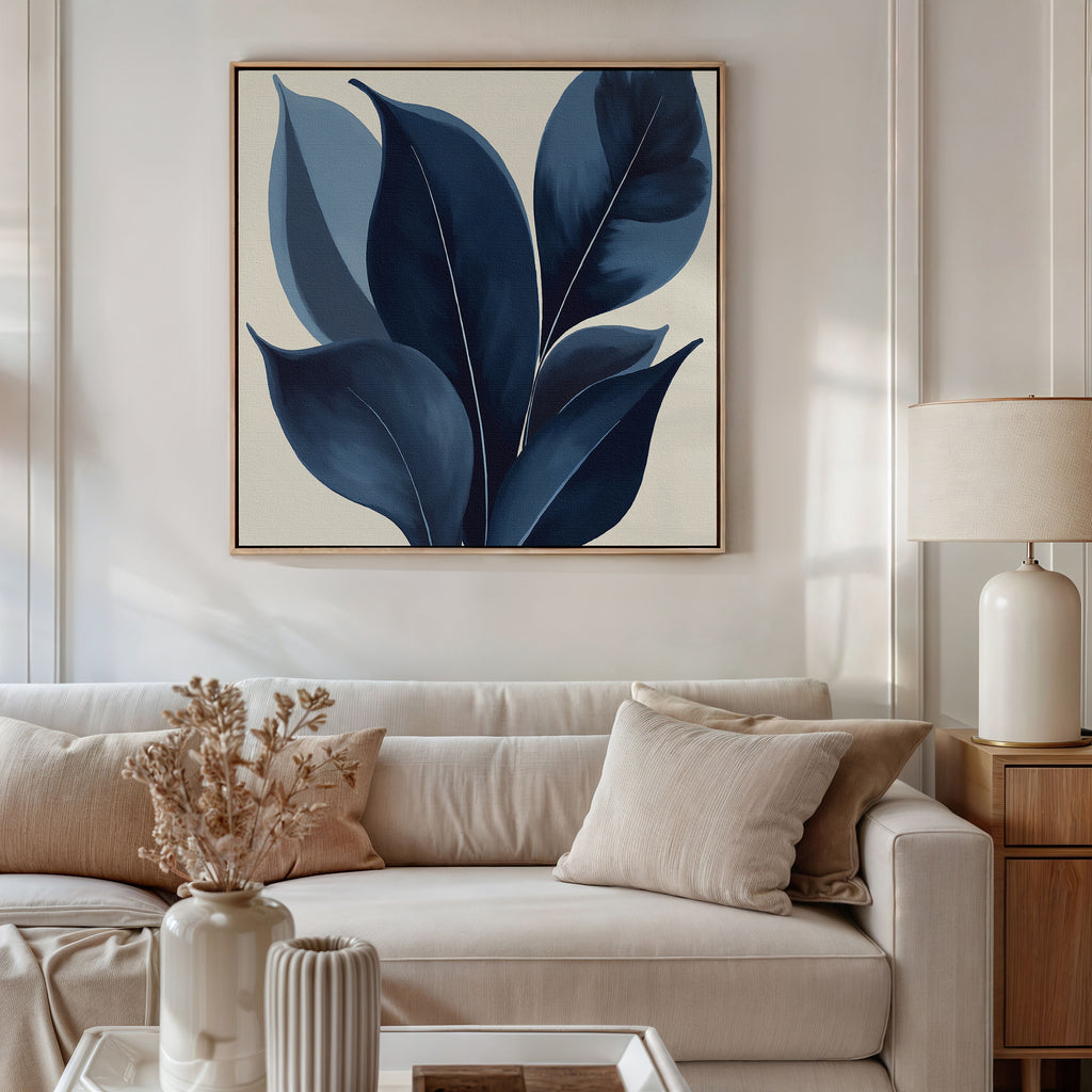A modern living room featuring a beige sofa, cream pillows, a light wooden side table with a lamp, and the Indigo Depths Canvas Art - Square hanging above the couch. Dried flowers in a vase add charm to the coffee table.