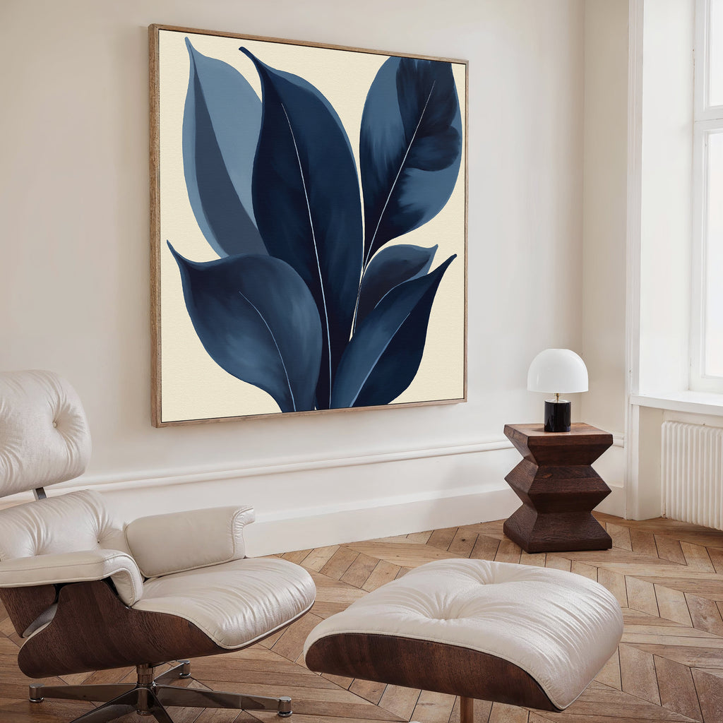 A modern living room with a tufted leather lounge chair and ottoman, a wooden geometric side table with a lamp, and elegant wall art—the Indigo Depths Canvas Art - Square—featuring blue abstract leaves above.
