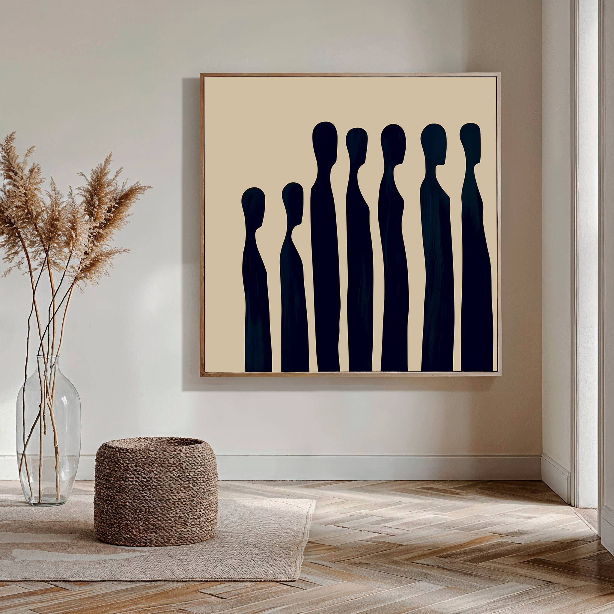 A modern living room showcasing the Indigo Profile Abstract Canvas Art—an abstract painting of elongated black figures on beige—paired with a woven ottoman and clear vase with dried pampas grass on a wooden floor.