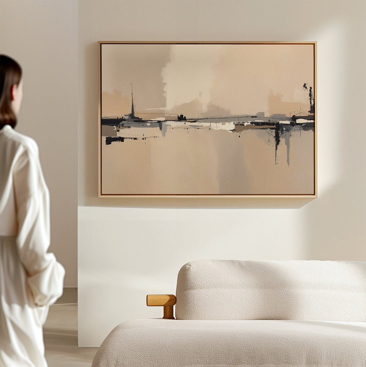 A woman in a white outfit stands in a minimalist room, admiring the Industrial Cityscape Canvas Art - Horizontal with beige, black, and gray tones hanging above a light-colored sofa.