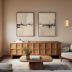 A modern living room showcases a wooden sideboard with a geometric pattern, a matching coffee table, neutral-toned armchairs, and the Industrial Cityscape - Set Of 2 art on the wall, plus a small vase with greenery on the table.