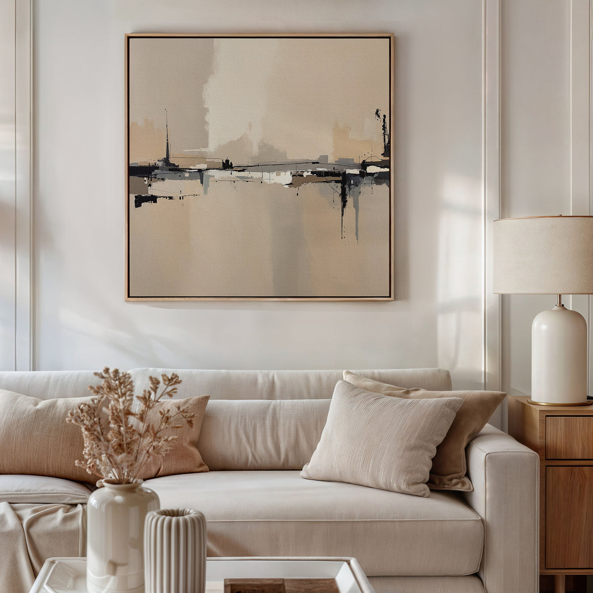 A neutral-toned living room featuring a beige sofa, cream and tan pillows, a wooden side table with lamp, dried flowers in vases, and the Industrial Cityscape Canvas Art - Square for modern wall decor in soft beige, black, and cream tones.