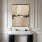 A minimalist console table with modern decor stands against a creamy paneled wall, topped by the Industrial Cityscape Canvas Art - Vertical, whose abstract city design in neutral tones adds sophistication to the elegant space.