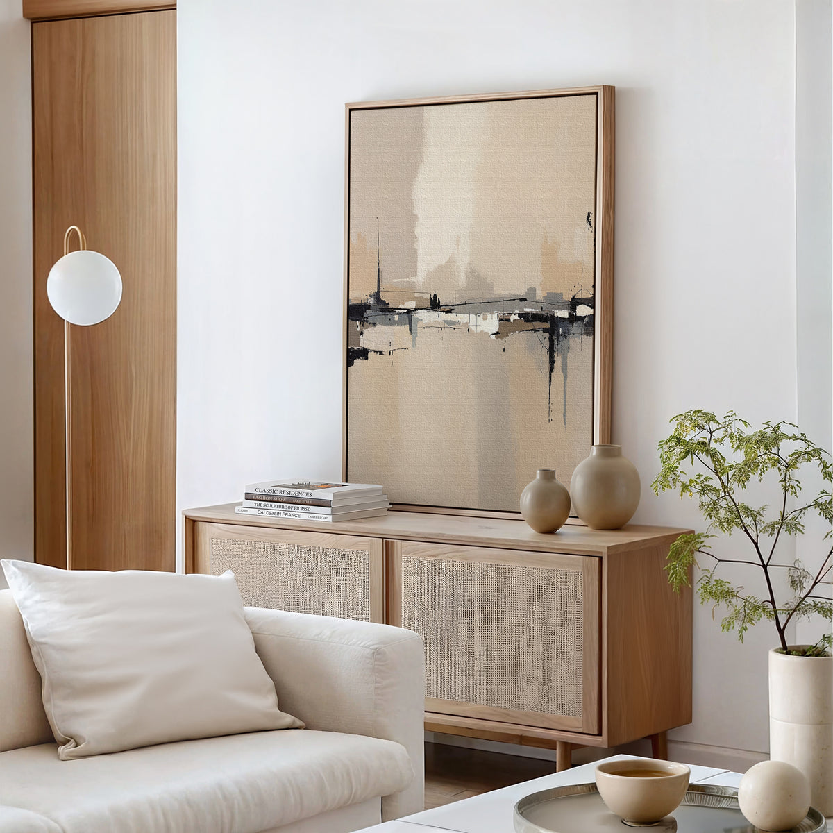 A modern living room in neutral tones showcases the Industrial Cityscape Canvas Art - Vertical, a light wood sideboard with vases and books, abstract wall art, a white sofa with cushions, a round coffee table, potted plant, and floor lamp.