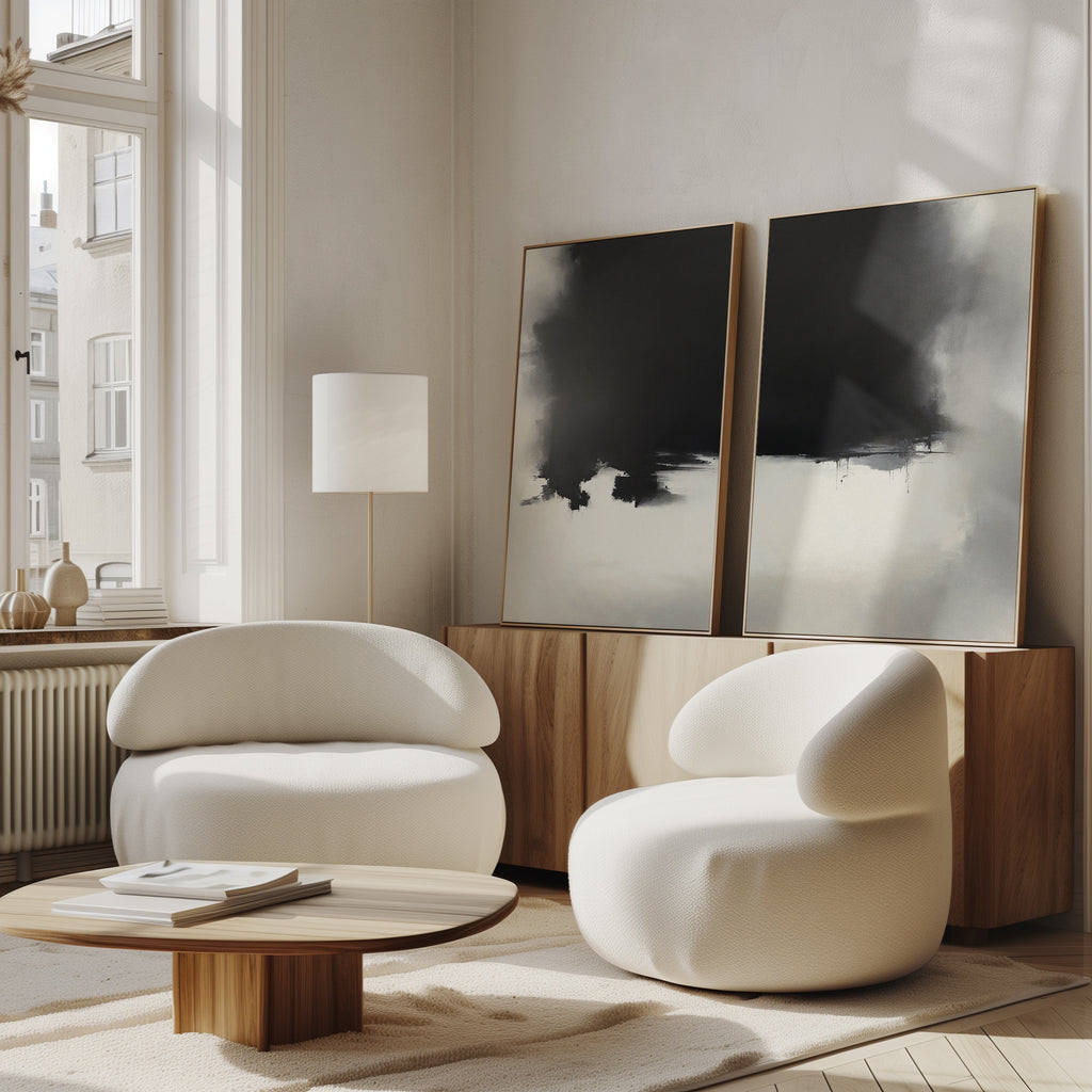 A modern living room with two curved white armchairs, a low wooden coffee table, and the Ink Cloud Formation - Set Of 2 monochrome art prints displayed on a wooden sideboard beneath tall windows.