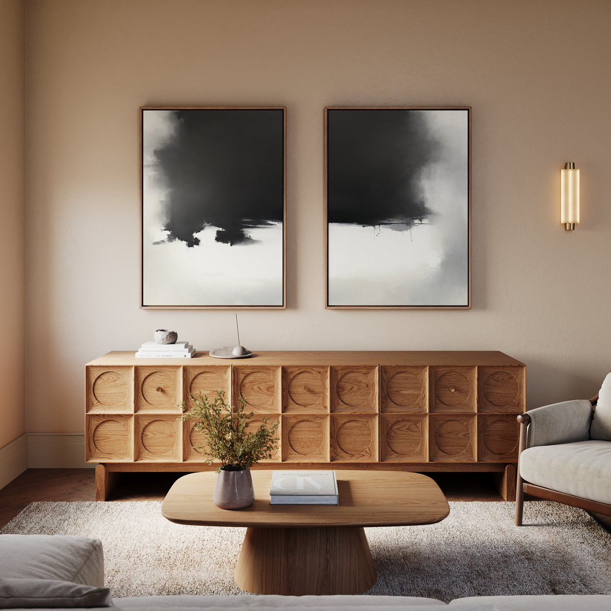 A cozy, modern living room featuring a wooden sideboard, a light-colored sofa, a wooden coffee table with books and a small vase with greenery, plus the Ink Cloud Formation - Set Of 2 black-and-white abstract prints on the wall.