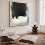 A modern living room with a white lounge chair, ottoman, geometric wood side table with lamp, and the Ink Cloud Formation Canvas Art – Square above herringbone wood floors creates modern sophistication.