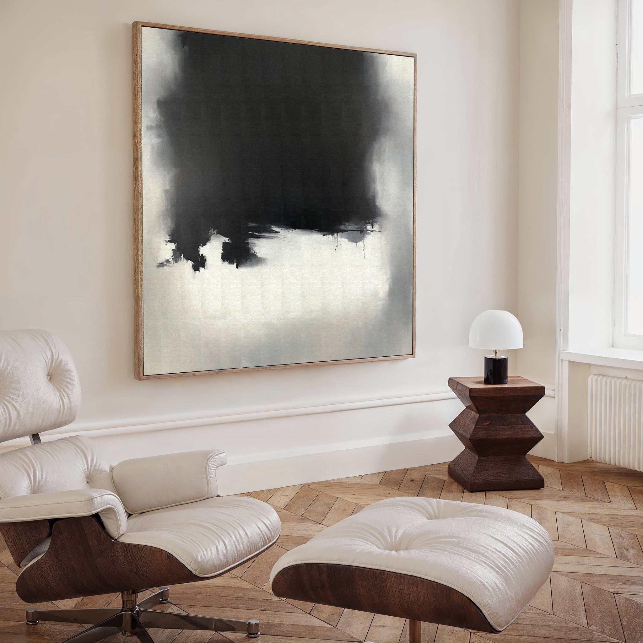 A modern living room with a white lounge chair, ottoman, geometric wood side table with lamp, and the Ink Cloud Formation Canvas Art – Square above herringbone wood floors creates modern sophistication.