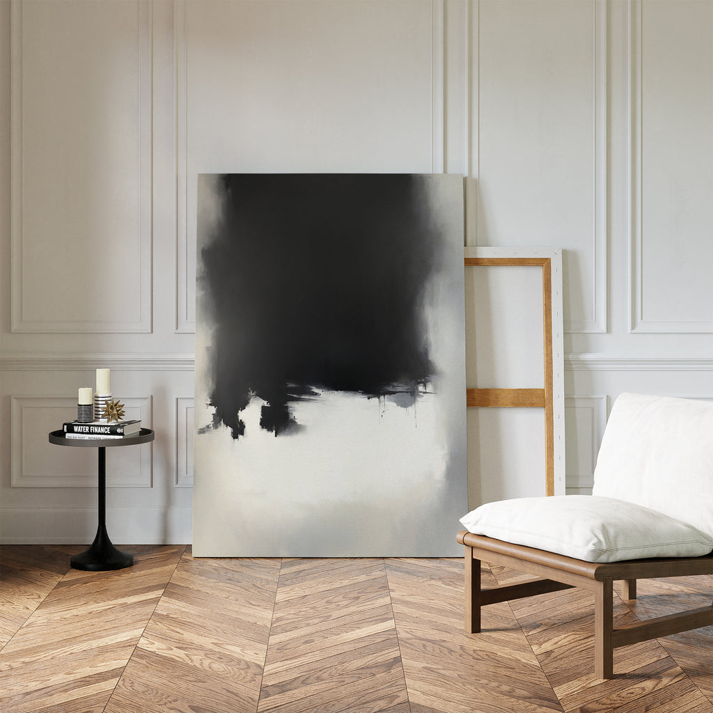 A minimal living room features a white cushioned chair, a round black side table with candles and books, and the Ink Cloud Formation Canvas Art - Vertical leaning against a white paneled wall with parquet wood flooring.