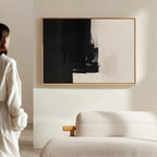 A person in a white shirt stands in a modern, minimal living room, admiring the Ink Divide Canvas Art - Horizontal displayed above a light-colored sofa.