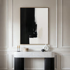Minimalist interior featuring the Ink Divide Canvas Art - Vertical, a large abstract black and white painting on a cream-paneled wall, paired with a marble console table and decorative objects for a refined, modern atmosphere.
