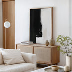Minimalist living room featuring the Ink Divide Canvas Art - Vertical, a light wood cabinet, neutral pottery, a small potted plant, a white sofa with cushions, and a modern floor lamp in the corner.