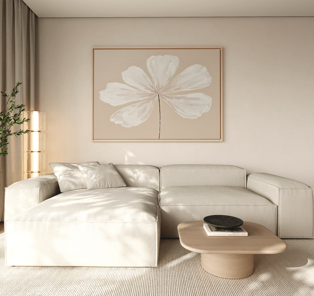A modern living room with a light beige sectional sofa, minimalist light wood coffee table with a black bowl, neutral rug, tall plant, and the Ivory Bloom Canvas Art - Horizontal as neutral wall decor above the seating area.