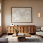 A modern living room with neutral tones showcases the Ivory Bloom Canvas Art - Horizontal above a wooden credenza, paired with a light wood coffee table, books, a beige sofa, and a wall sconce for a calm, minimalist vibe.