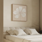 A neutral-toned bedroom features a beige upholstered bed, white bedding, and the Ivory Bloom Canvas Art - Square above the headboard. A bare branch in a vase adds a final touch of neutral decor to the bedside table.